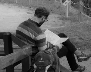 Kolumnist Franz von hinten, das Foto ist schwarzweiß, er sitzt auf einer Bank und liest eine Karte