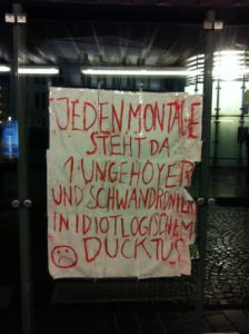Ein Plakat, darauf steht: "Jeden Montage steht da 1 Ungehoyer und schwandroniert in idiotlogischem Ducktus", daneben ein trauriger Smiley
