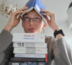 luhze-Autor Eric Binnebößel mit einem Stapel Bücher, von denen er eins auf dem Kopf balanciert