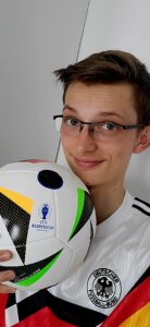 Porträtfoto des Autors. Er trägt das Deutschland-Trikot von 1990 und hält den Spielball der EM 2024 in der rechten Hand.