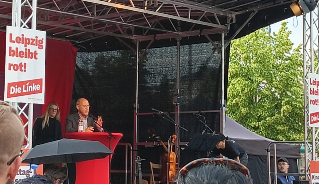 Gregor Gysi steht auf einer Bühne und hält eine Rede. Vor ihm ein Stehtisch in rot. 